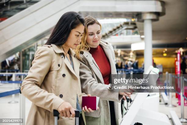 two women use check-in kiosk in airport - long coat stock pictures, royalty-free photos & images