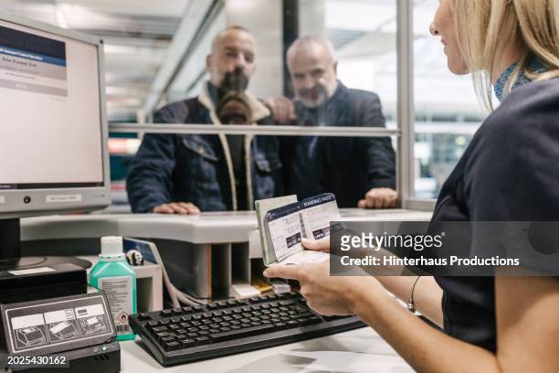 airport staff member checking passenger's details while helping them check in for a flight - german passports stock-fotos und bilder