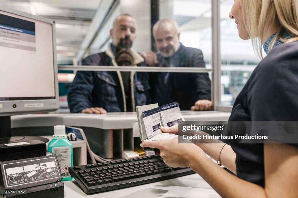 Airport Staff Member Checking Passenger's Details While Helping Them Check In For A Flight