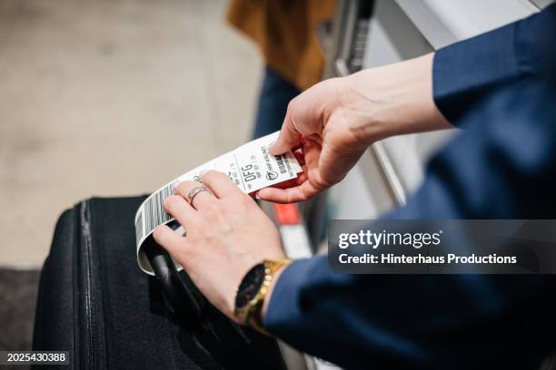 close up of airport staff member attaching tag to passenger's luggage - étiquette de bagage photos et images de collection