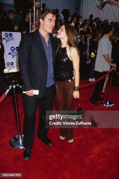 American actor Chris Noth, wearing a black suit over a blue shirt, and American actress Kristin Davis, who wears a black sequin halter top and brown...