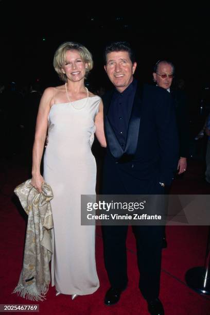 American singer, songwriter and actor Mac Davis, wearing a tuxedo over a black shirt, and his wife, Lise, who wears an asymmetric white evening gown,...