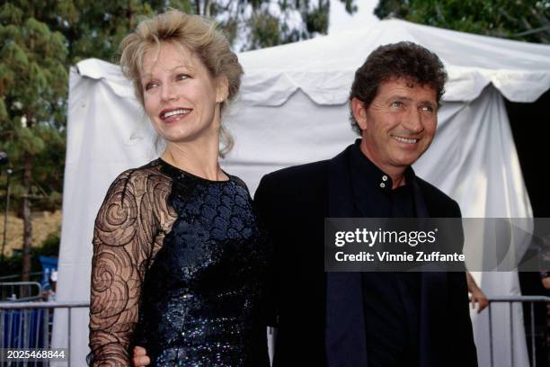 American singer, songwriter and actor Mac Davis, wearing a tuxedo over a black shirt, and his wife, Lise, who wears a black sequin outfit with sheer...