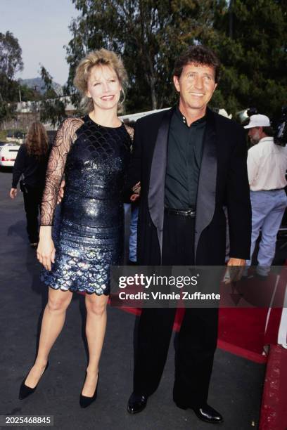 American singer, songwriter and actor Mac Davis, wearing a tuxedo over a black shirt, and his wife, Lise, who wears a black sequin outfit with sheer...