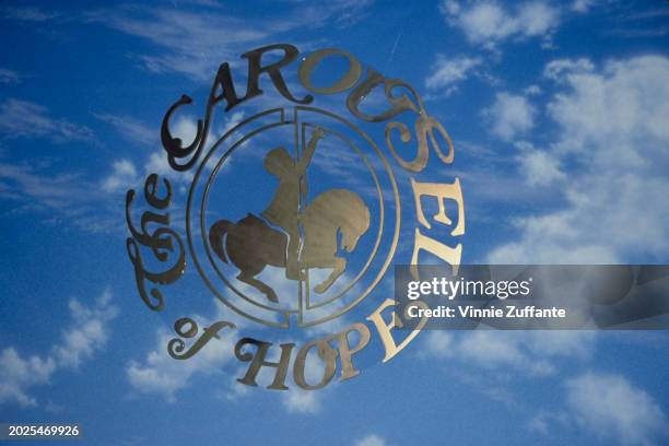 Backdrop sign at a Carousel of Hope Ball, depicting a silhouette of a child riding a carousel against a background of blue sky and clouds, United...