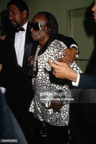 American trumpeter and composer Miles Davis, wearing sunglasses and a silver-and-black jacket, attends the 1987 Soul Train Music Awards, held at the...