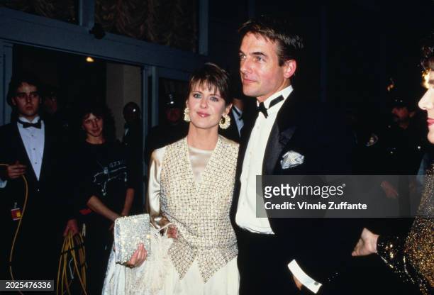 American actress Pam Dawber, wearing a white evening gown with a gold checked waistcoat, and American actor Mark Harmon, who wears a tuxedo and bow...