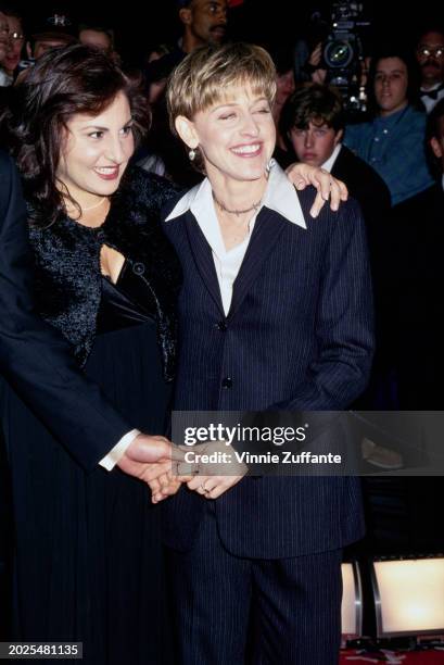 American actress Kathy Najimy, wearing a black outfit, her left arm around American television host and comedian Ellen DeGeneres, who wears a dark...