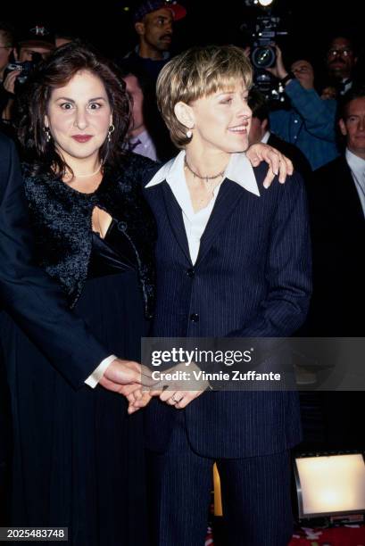 American actress Kathy Najimy, wearing a black outfit, her left arm around American television host and comedian Ellen DeGeneres, who wears a dark...