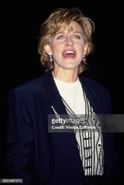American television host and comedian Ellen DeGeneres, wearing a dark blue blazer over a black macrame waistcoat, over a white crew neck top, attends...