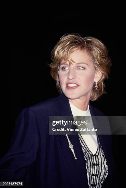 American television host and comedian Ellen DeGeneres, wearing a dark blue blazer over a black macrame waistcoat, over a white crew neck top, attends...