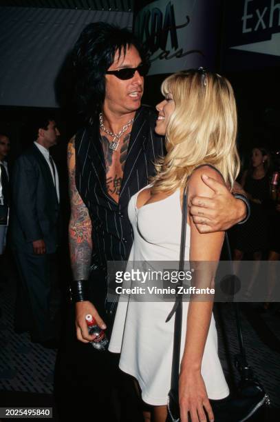 American bass player Nikki Sixx, wearing a pinstripe black vest and sunglasses, and his wife, American actress and glamour model Donna D'Errico, who...