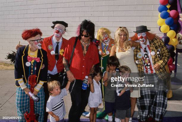 American bass player Nikki Sixx, wearing a red short-sleeved shirt and sunglasses, and his wife, American actress and glamour model Donna D'Errico,...