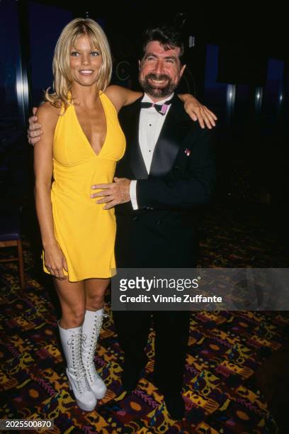 American actress and glamour model Donna D'Errico, wearing a yellow dress with white knee-high boots, and American screenwriter Michael Berk, who...