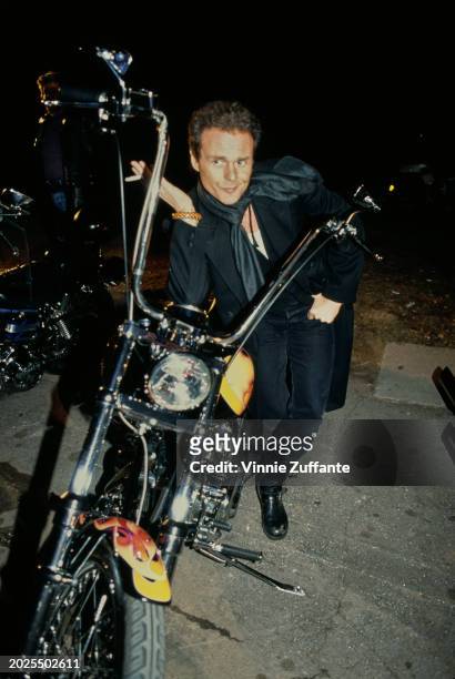 British actor and singer Michael Des Barres, wearing a black suit with a black scarf, poses beside a motorcycle at the IFP 'Rebel With A Cause'...