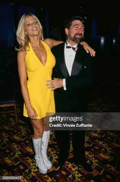 American actress and glamour model Donna D'Errico, wearing a yellow dress with white knee-high boots, and American screenwriter Michael Berk, who...