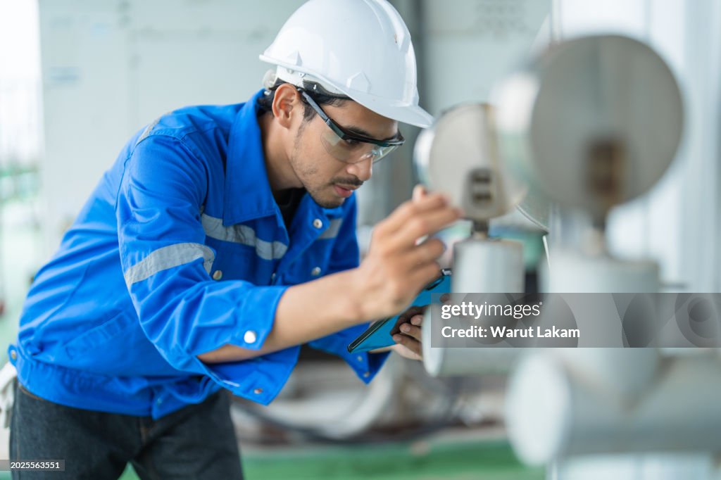 Professional industrial worker or engineer closely examining gauge readings and analyzes data on tablet during machinery inspection for quality control