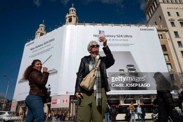 Woman uses a mobile phone to take images in front of an advertising banner, ahead of the Mobile World Congress , in Barcelona on February 23, 2024....