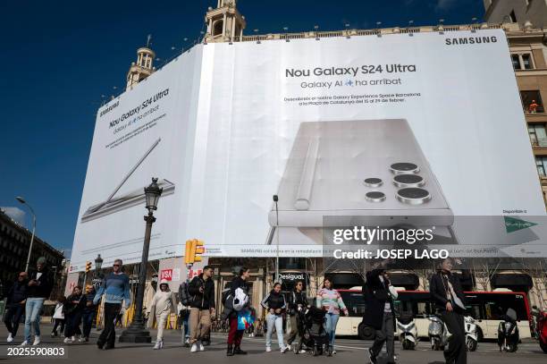 People walk past a building wrapped in an advertising banner, ahead of the Mobile World Congress , in Barcelona on February 23, 2024. The world's...