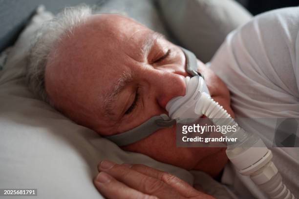 mature man sleeping with a cpap (continuous positive airway pressure) machine after being diagnosed with sleep apnea - bruxism stock pictures, royalty-free photos & images