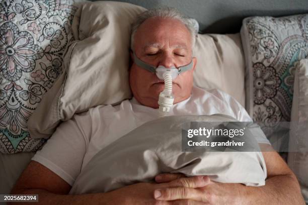 mature man sleeping with a cpap (continuous positive airway pressure) machine after being diagnosed with sleep apnea - bruxism stockfoto's en -beelden