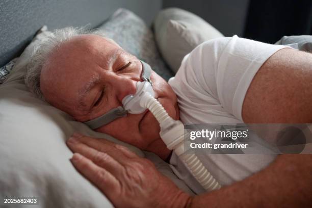 mature man sleeping with a cpap (continuous positive airway pressure) machine after being diagnosed with sleep apnea - bruxism stock pictures, royalty-free photos & images