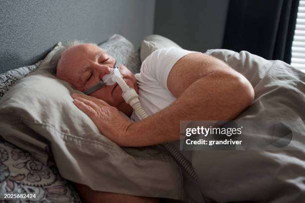 mature man sleeping with a cpap (continuous positive airway pressure) machine after being diagnosed with sleep apnea - bruxism stock pictures, royalty-free photos & images