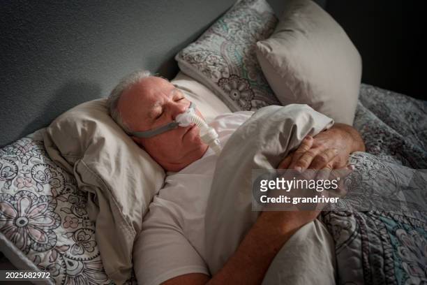 mature man sleeping with a cpap (continuous positive airway pressure) machine after being diagnosed with sleep apnea - bruxism stockfoto's en -beelden