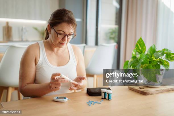 mature hispanic woman measuring glucose sitting at home - glucose stockfoto's en -beelden