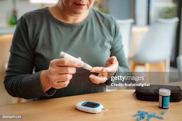 mature diabetic woman checking blood sugar level at home - glucose stockfoto's en -beelden