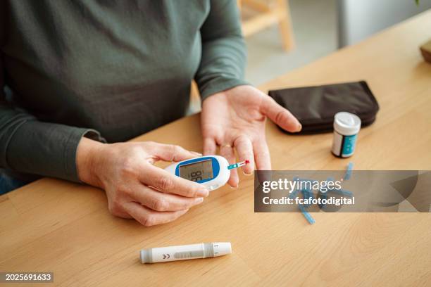 mujer diabética usa glucómetro para controlar su nivel de glucosa en casa - diabetes fotografías e imágenes de stock