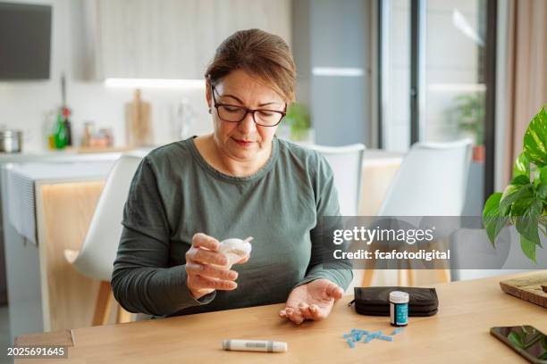 mature diabetic woman reading glucose level on glucometer - glucose stockfoto's en -beelden