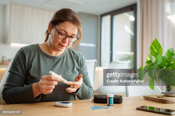 mature diabetic woman using lancet on finger for checking blood sugar level by glucose meter - medical glucometer stock pictures, royalty-free photos & images