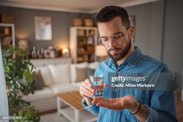 el joven toma medicamentos para reducir la depresión o los dolores de cabeza - tomar medicina fotografías e imágenes de stock
