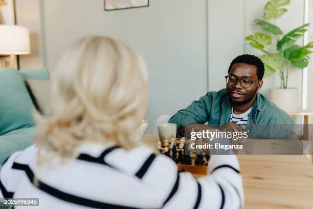 couple in love sitting on a living room floor, playing chess and having fun - chess stock pictures, royalty-free photos & images