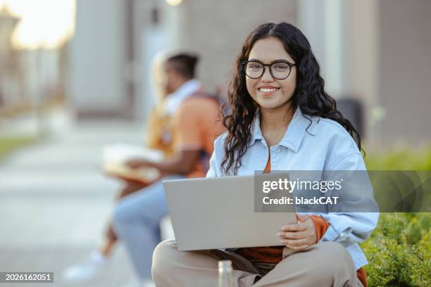 portrait of a young latin female student using laptop on the bench on campus - universiteitsstudent stockfoto's en -beelden