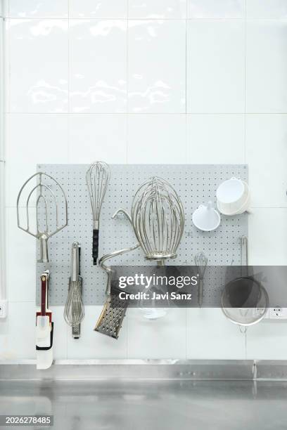 vertical photo of a modern set of utensils kitchenware and mixer attachments hanging on wall in light kitchen of bakery and cake shop - funnel cake stock pictures, royalty-free photos & images