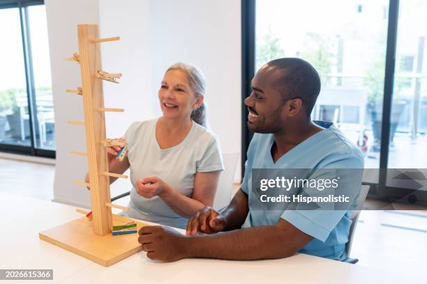 cheerful senior woman in occupational therapy with a black male patient having fun - occupational therapy stock pictures, royalty-free photos & images