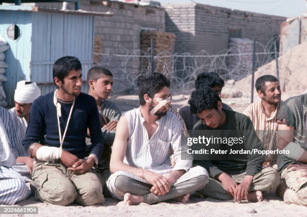 Wounded Iranian prisoners of war sitting on the ground in Basra, Iraq, during the Iran-Iraq War, circa March 1984.