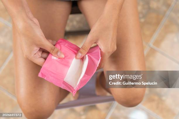 young woman with menstruation opening a pad to put it on - menstruation photos et images de collection