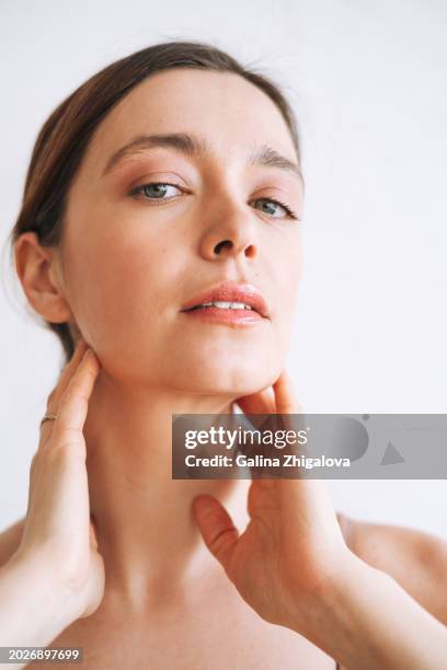 vertical beauty portrait of young woman with clear healthy skin and hands on her face against white backdrop - natural portrait studio shot white background stock pictures, royalty-free photos & images