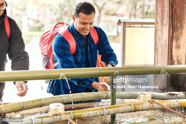 ethnic indian man purifies his hands at a temple's hand-watering fountain. - bamboo dipper - fotografias e filmes do acervo