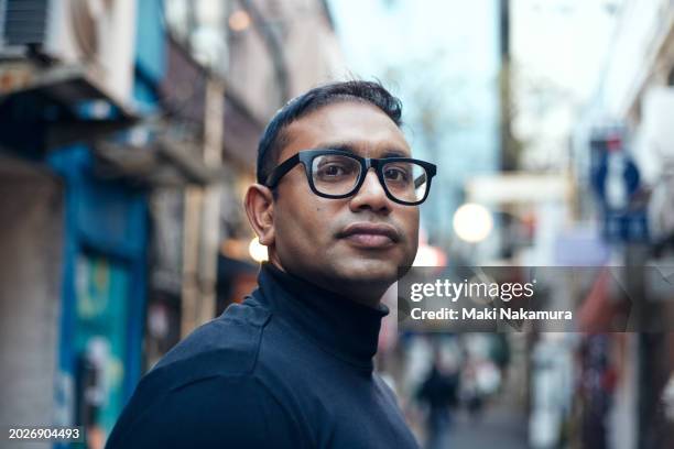 smiling ethnic indian male traveler strolls through downtown tokyo at night. - illuminated portrait stock pictures, royalty-free photos & images