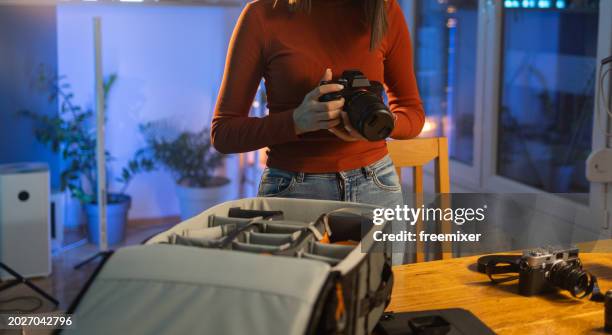 young woman packing her photographic equipment in professional camera bag in studio - camera bag stock pictures, royalty-free photos & images