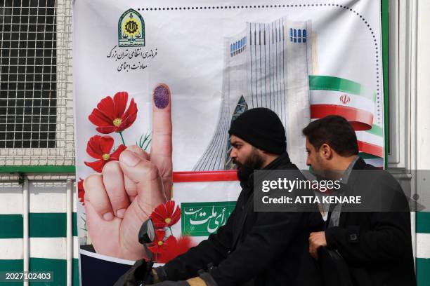 Men ride their scooter in front of a poster encouraging Iranians to vote in the upcoming elections, in Tehran on February 24, 2024. Voters are due to...