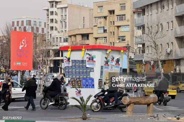 People drive past an installation in the form of a giant ballot box bearing electoral campaign posters, ahead of the upcoming elections, in Tehran on...