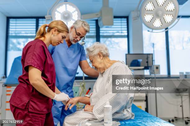 nurse and doctor preparing elderly patient for surgery, inserting iv cannula in her hand. - inserting iv stock pictures, royalty-free photos & images