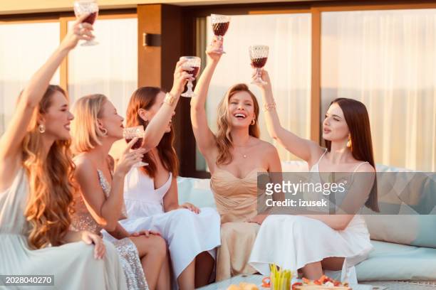 female friends wearing elegant dresses drinking wine outdoors at sunset - long dress party stock pictures, royalty-free photos & images