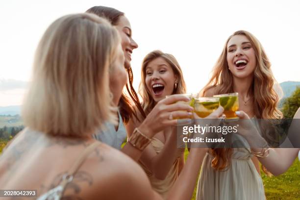 female friends wearing elegant dresses holding mojito drinks outdoors at sunset - bachelorette stock pictures, royalty-free photos & images