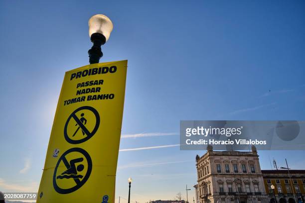Do Not Bathe" sign hangs from a lamp post in Cais das Colunas, Terreiro do Paço, by the Tagus River, a favorite tourist spot, on February 19 in...